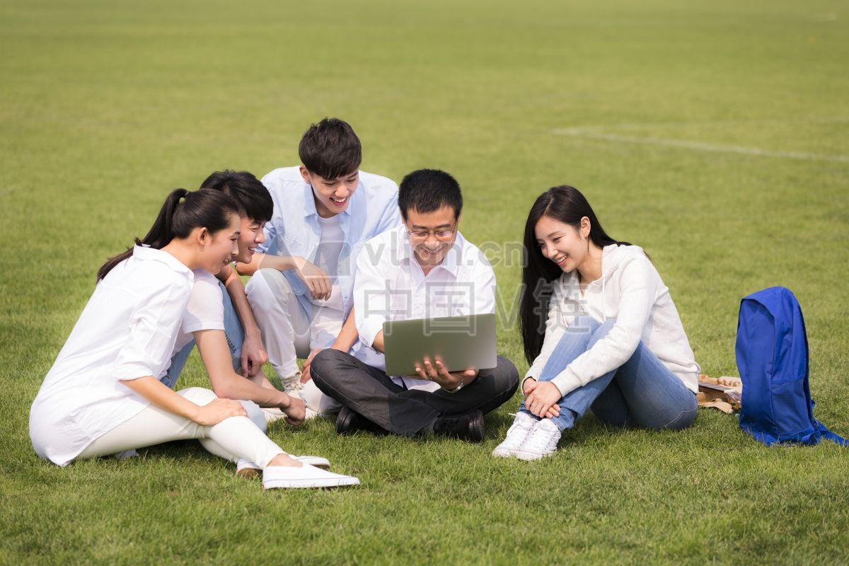 穿着绿色球鞋的社会团体成员在草坪上微笑着使用笔记本电脑上网本